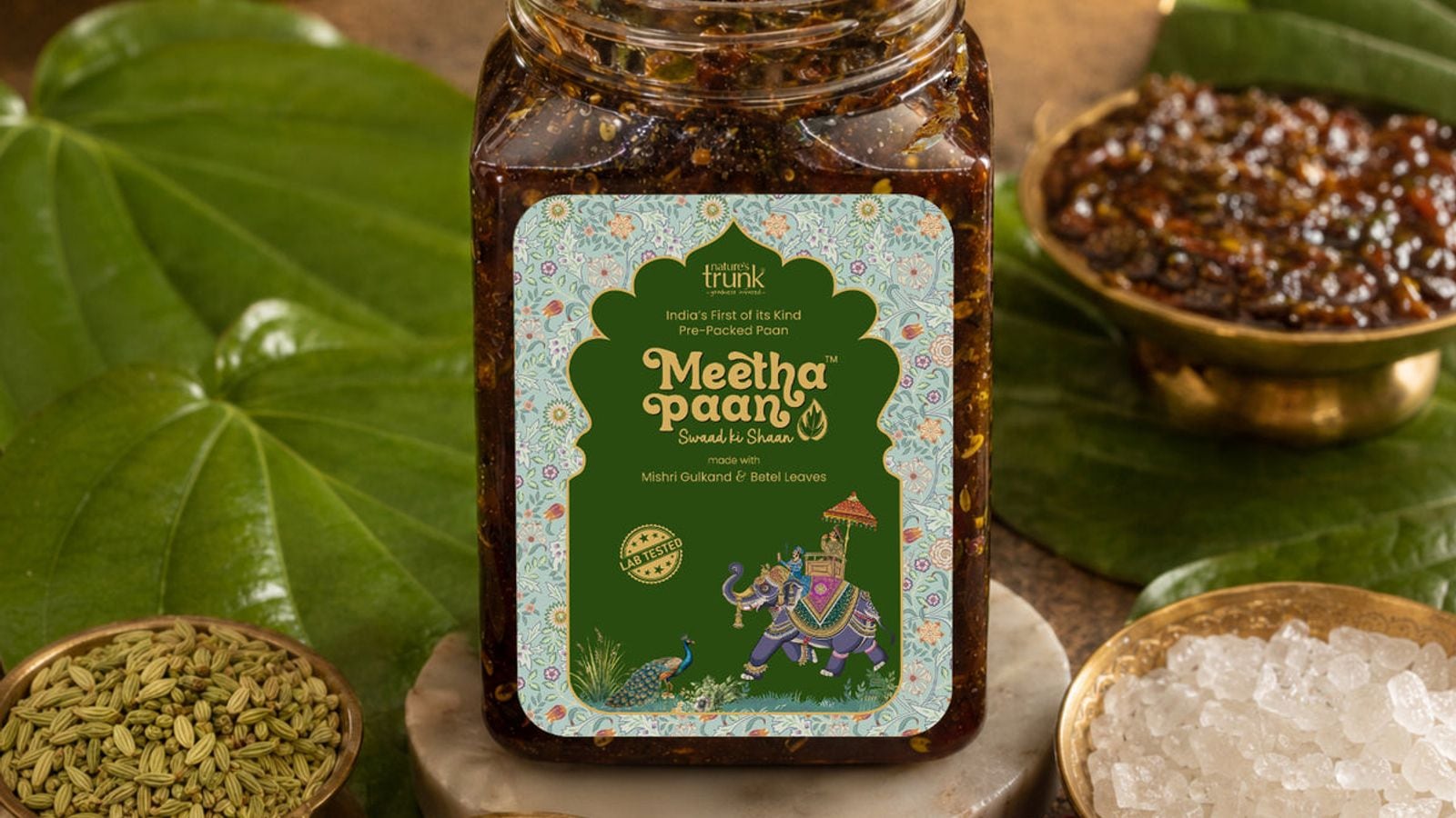 A jar of Nature’s Trunk Meetha Paan on betel leaves with bowls of fennel seeds and rock sugar