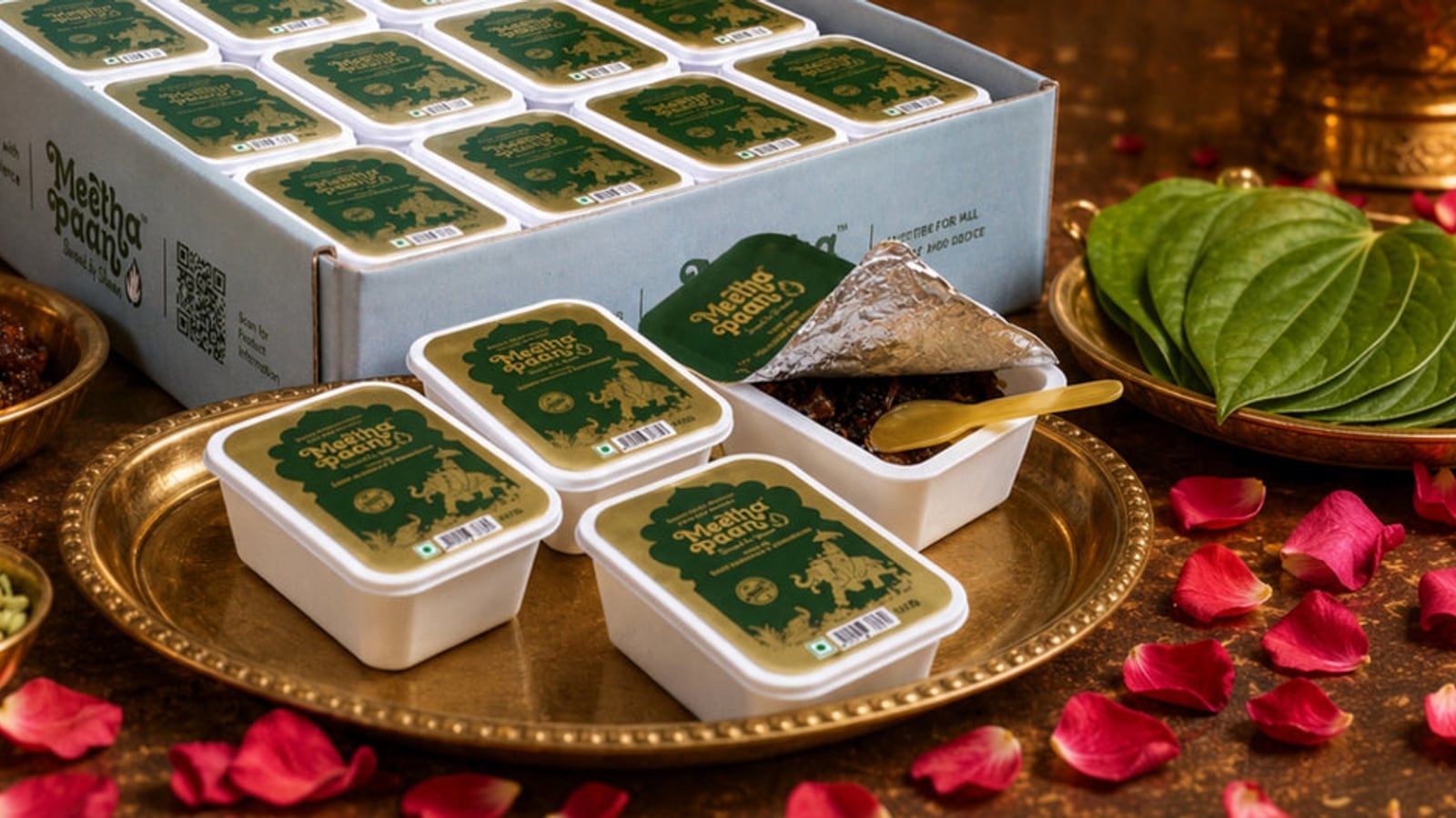 A Meetha Paan party box of individually packed portions on a brass platter with rose petals and diyas, ready for a wedding celebration
